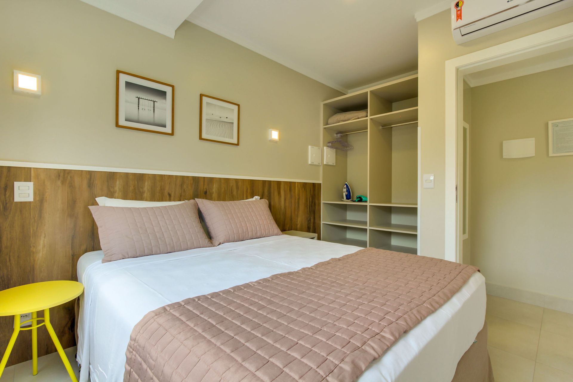 Quarto com cama, guarda-roupa e mesa de cabeceira amarela. Decoração em tons terrosos.