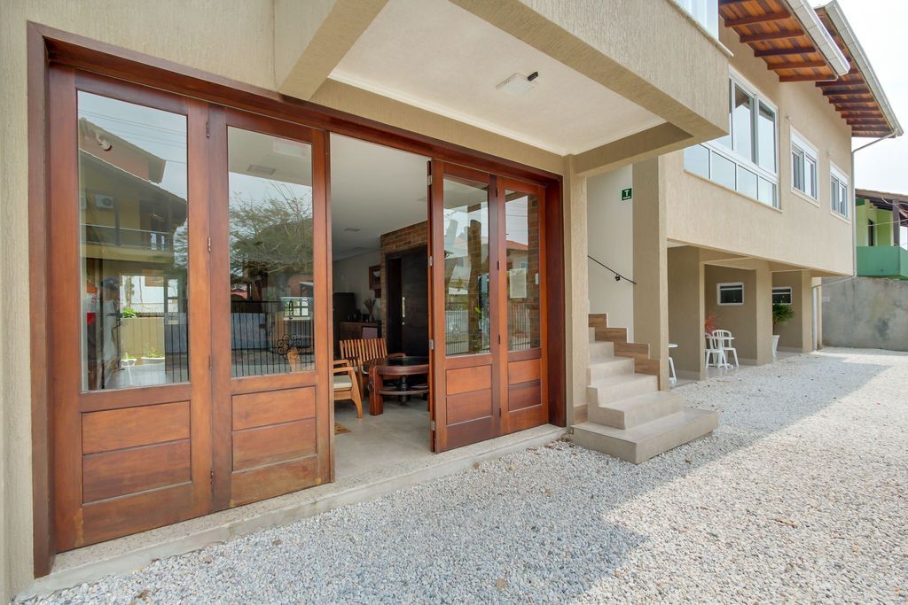 Portas dobráveis ​​abertas revelam um espaço interior de convivência. Móveis de madeira estão dispostos sobre um piso de cor clara.