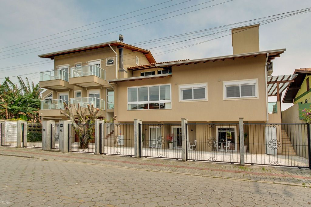 Casa bege de dois andares com varanda e cerca de ferro, sob um céu nublado.