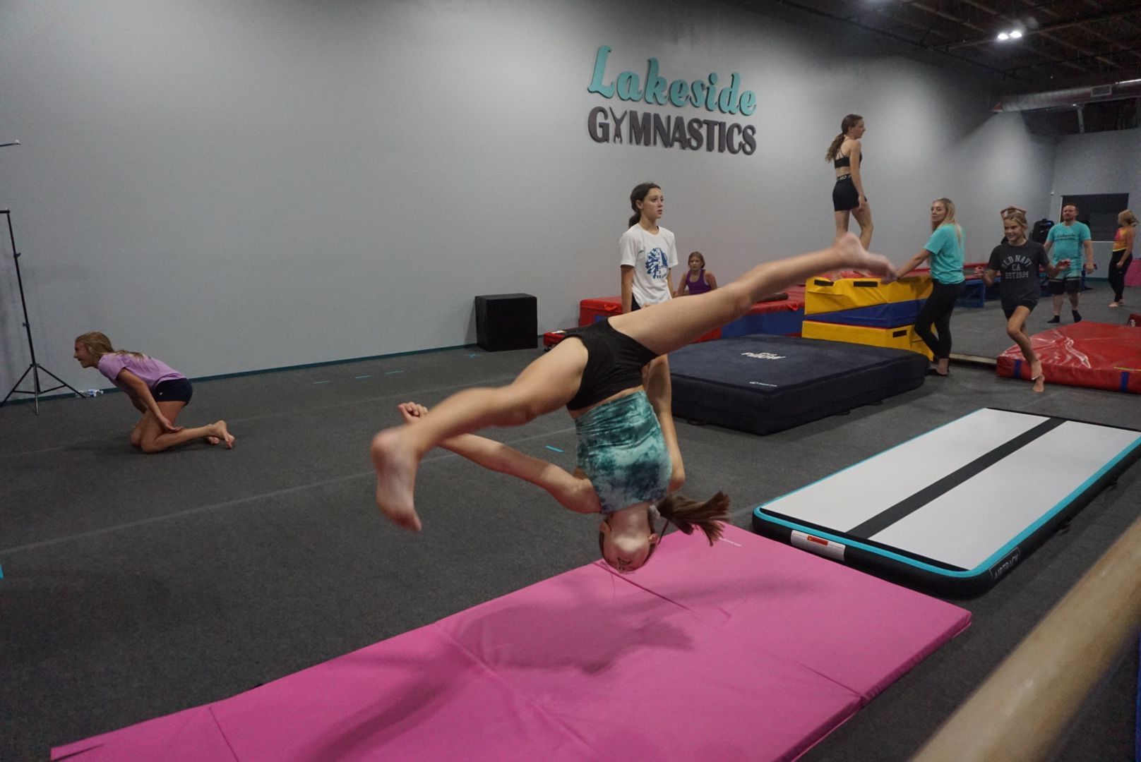 A girl is doing a handstand on a pink mat in a gym.