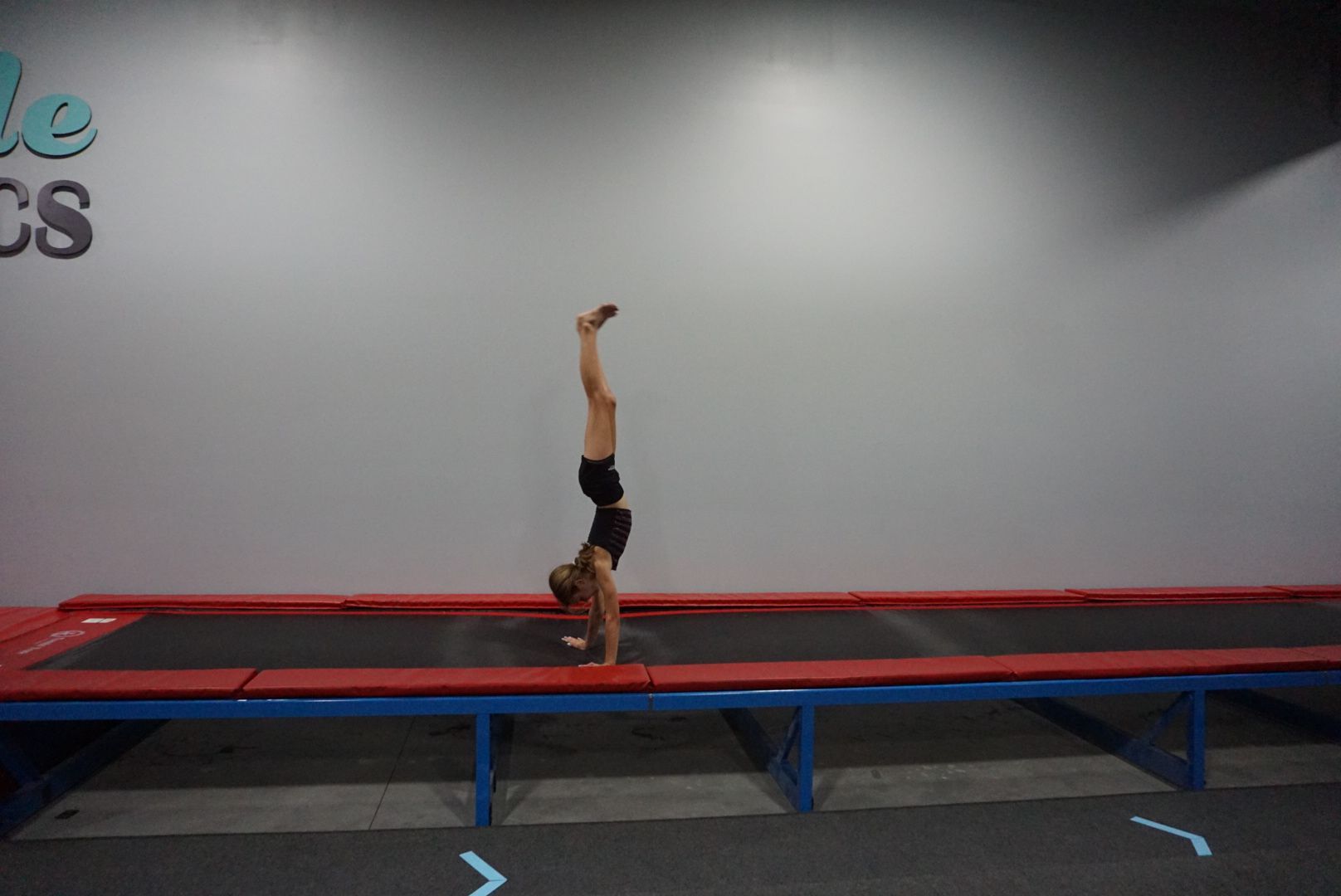 A person is doing a handstand on a trampoline in front of a wall that says cs