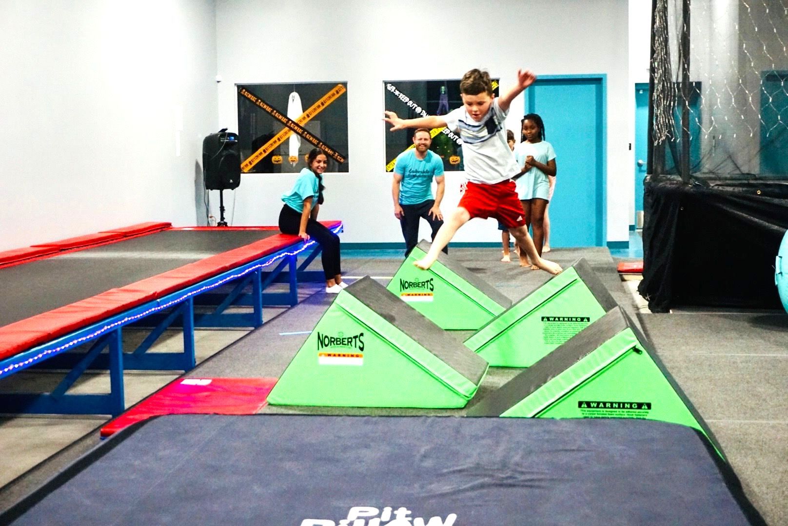 A young boy is jumping over a balance beam in a gym.