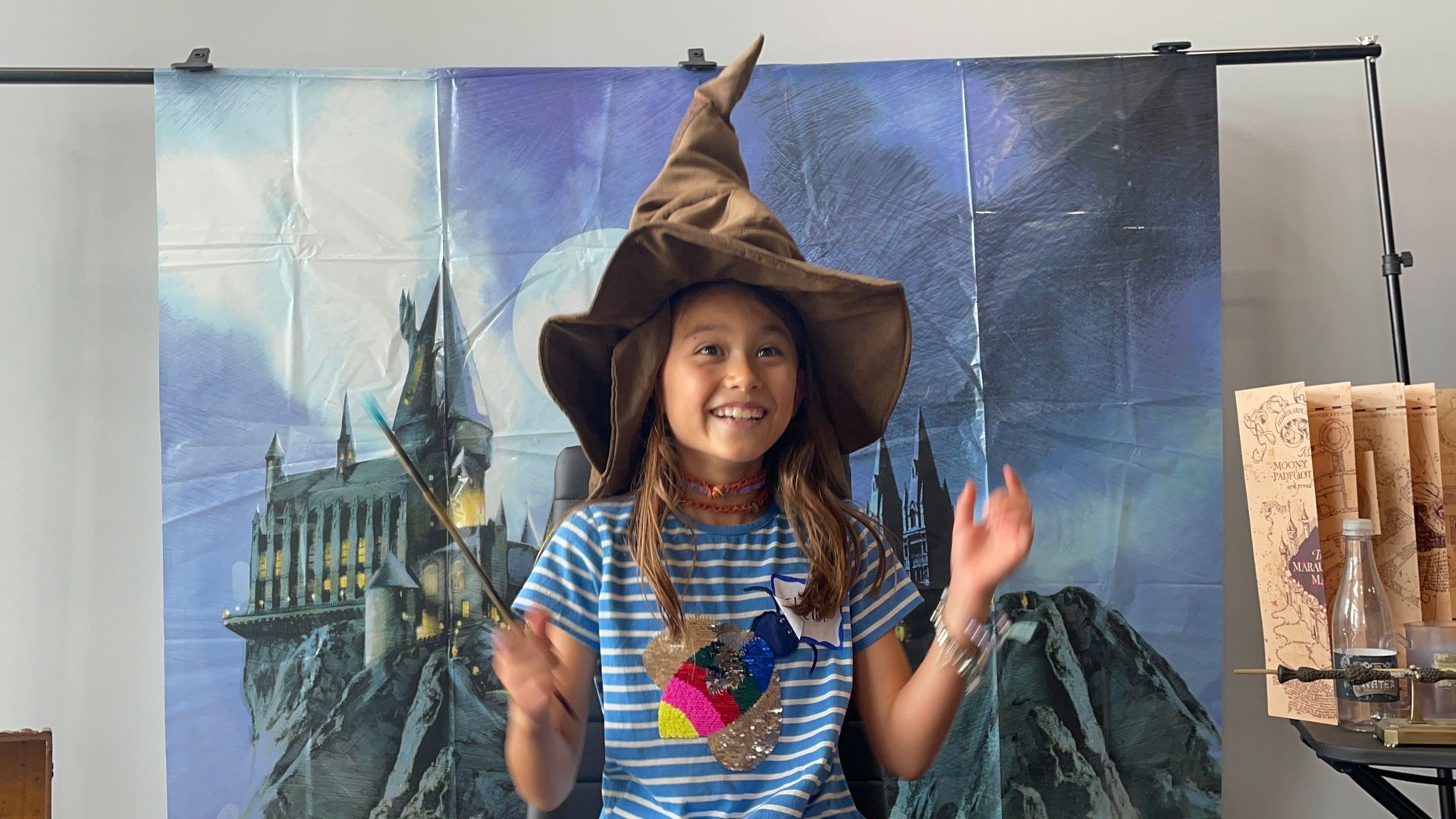 A little girl is wearing a wizard hat and holding a wand.