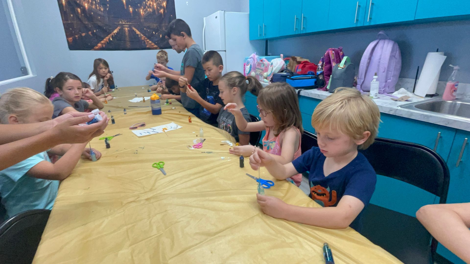 A group of children are sitting at a long table in a kitchen.