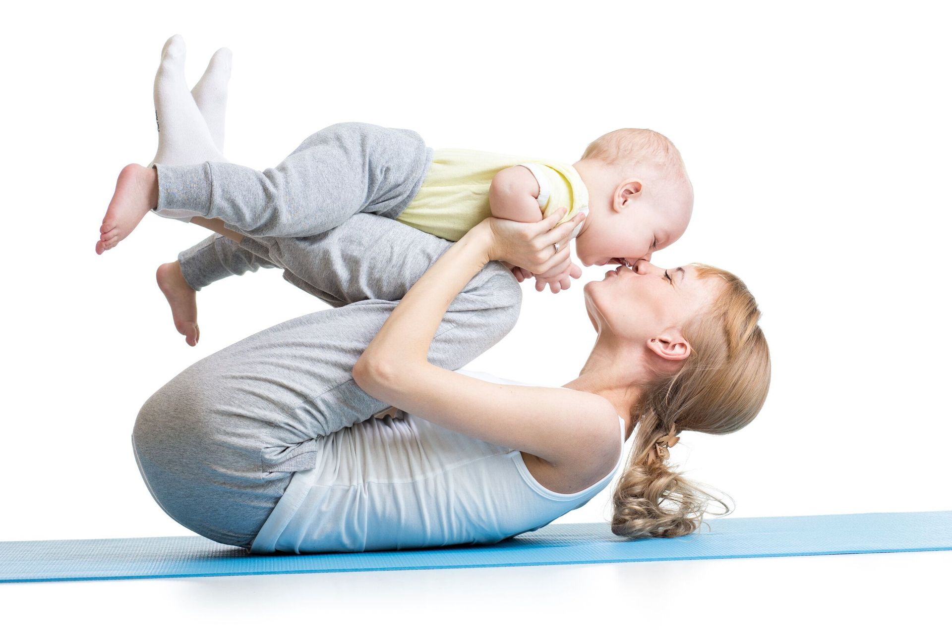 A woman is laying on a yoga mat holding a baby in her arms.