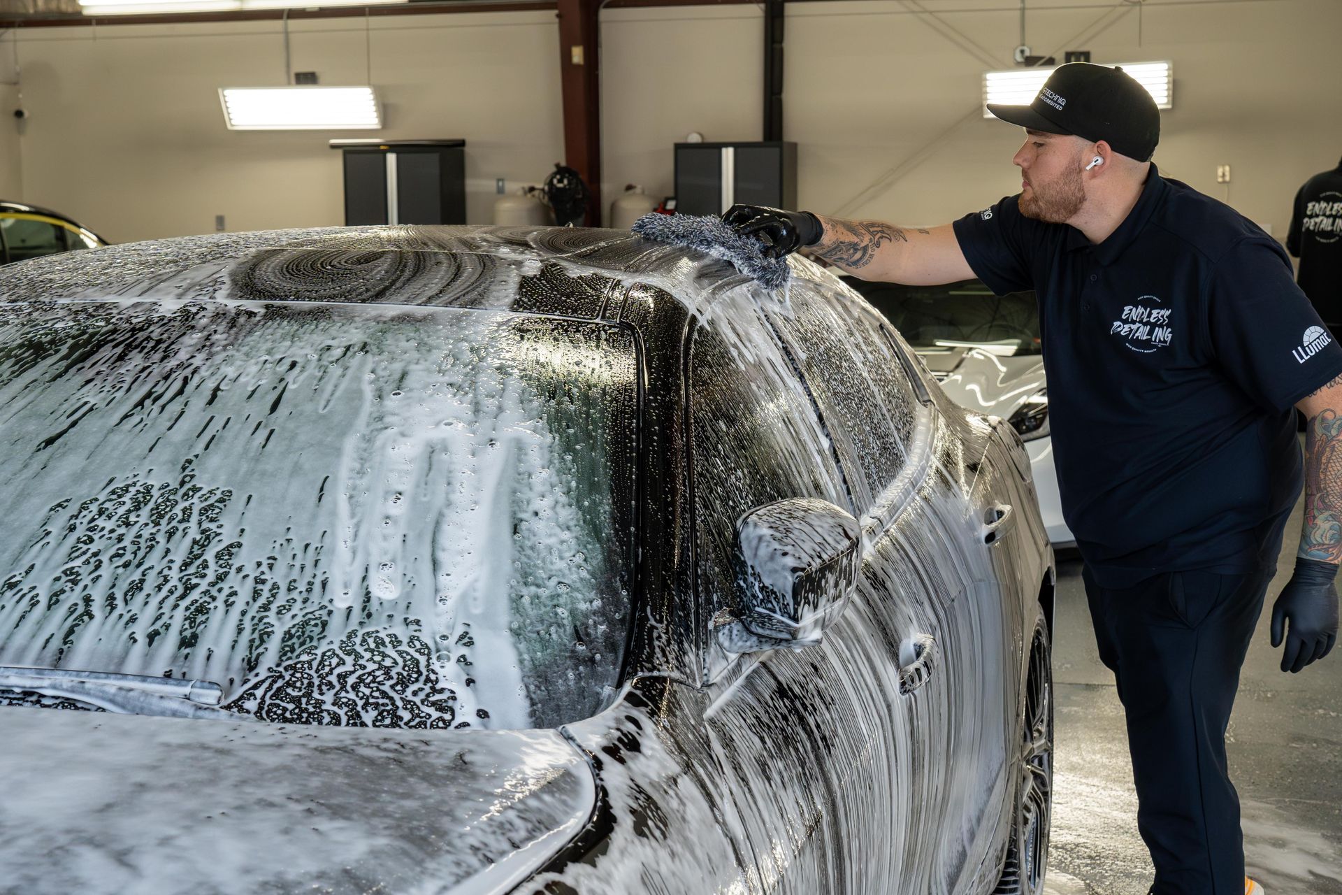 Man washing a car with soap in a garage.