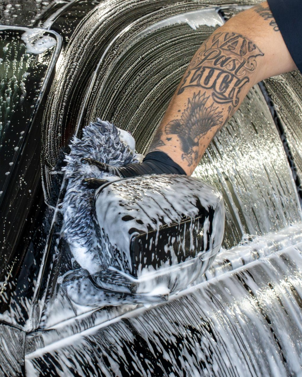 A man is cleaning the wheel of a black car with a sponge.