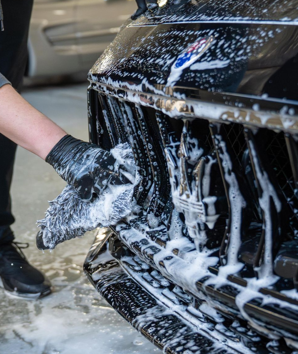A man is cleaning the wheel of a black car with a sponge.