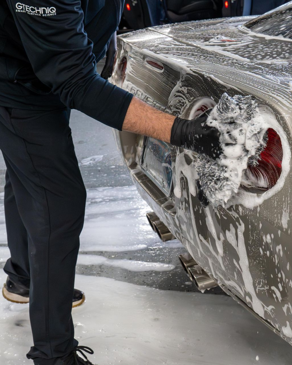 A person wearing black gloves is polishing a black car