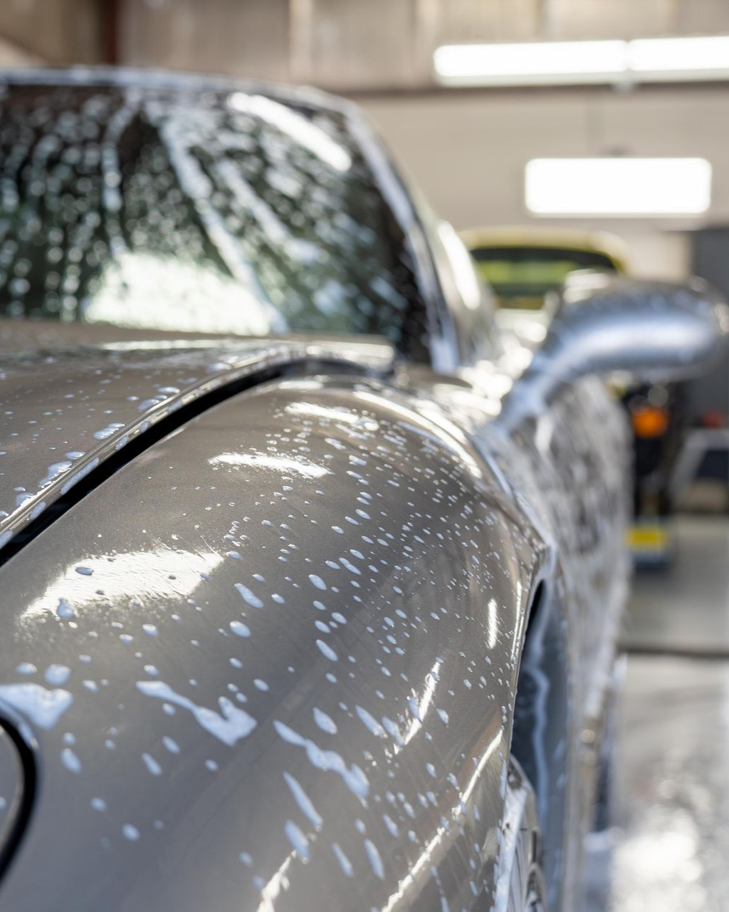 Person washing a black car covered in soap suds with a sponge
