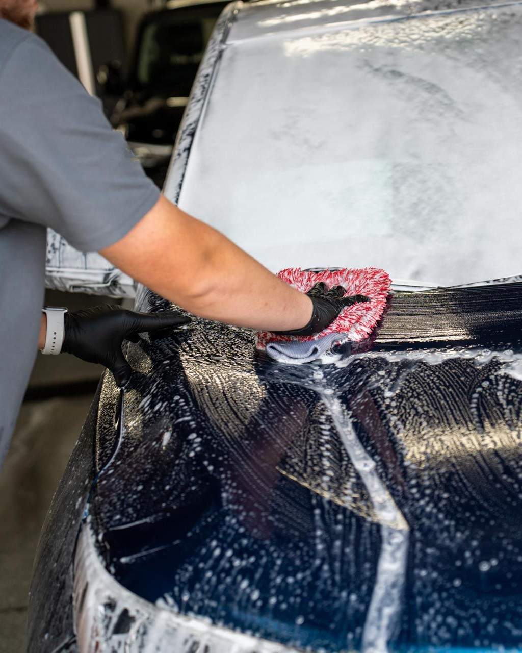 Person washing a blue car with a soapy sponge at a car wash.