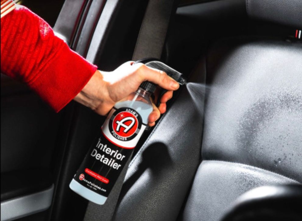 Hand spraying interior detailer onto a black car seat