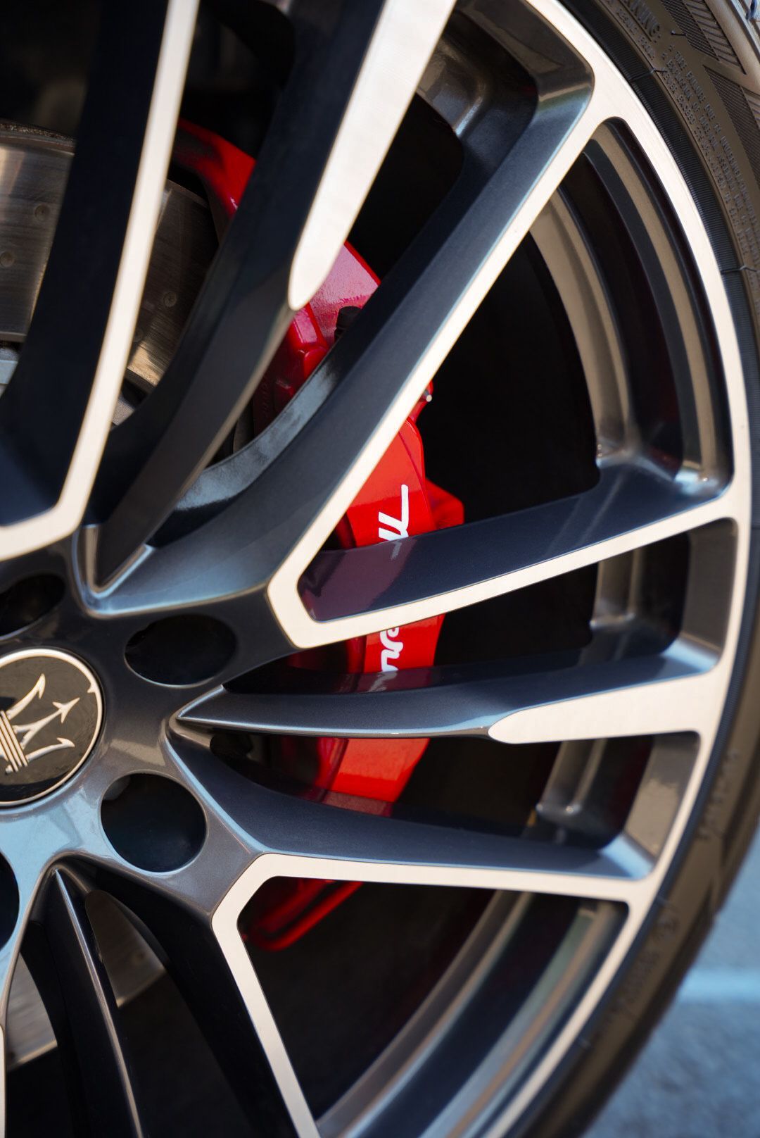 Close-up of a Maserati car wheel with a red brake caliper, showing the brand's logo.
