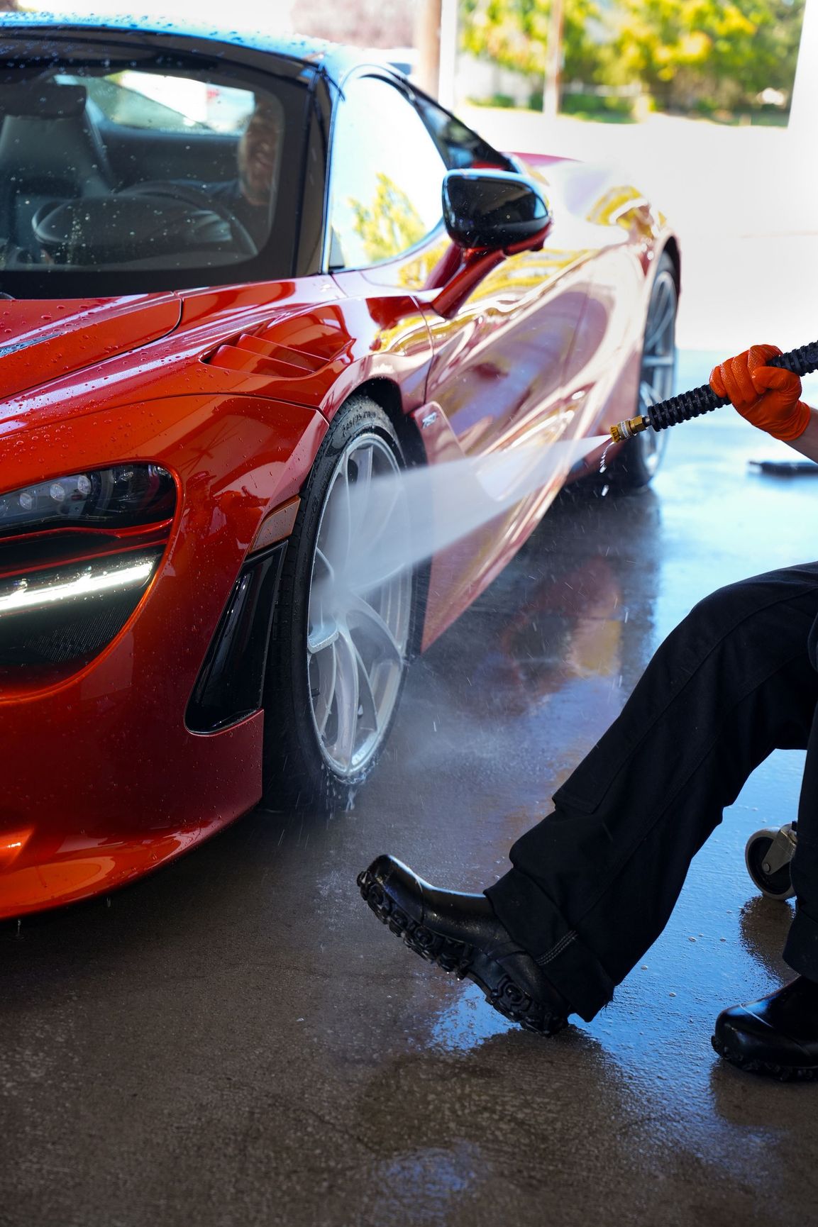 Person pressure-washing a red sports car at a car wash