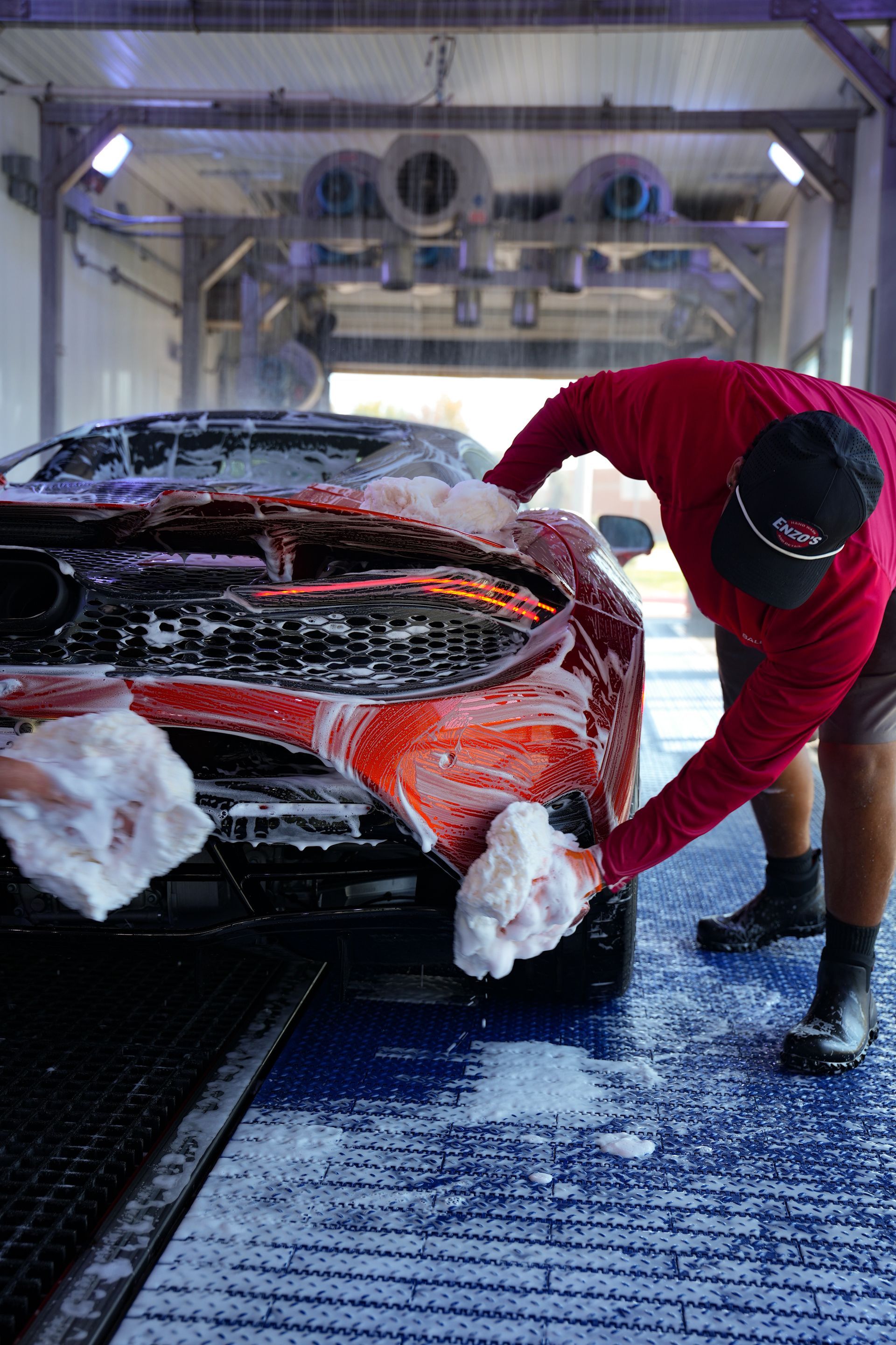 Person washing a red car in a car wash, applying soap to the front bumper.