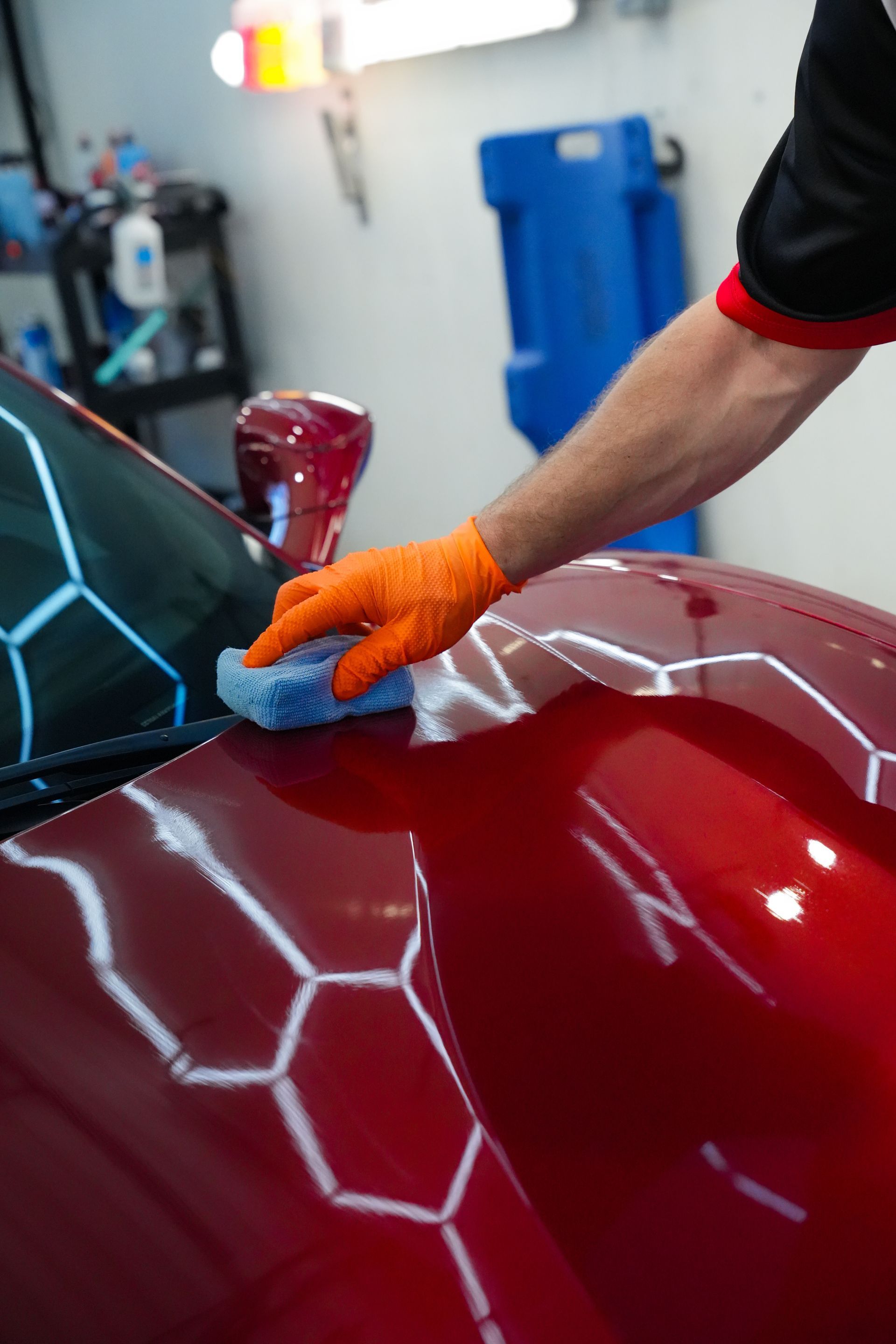 A man is polishing a red sports car in a garage.