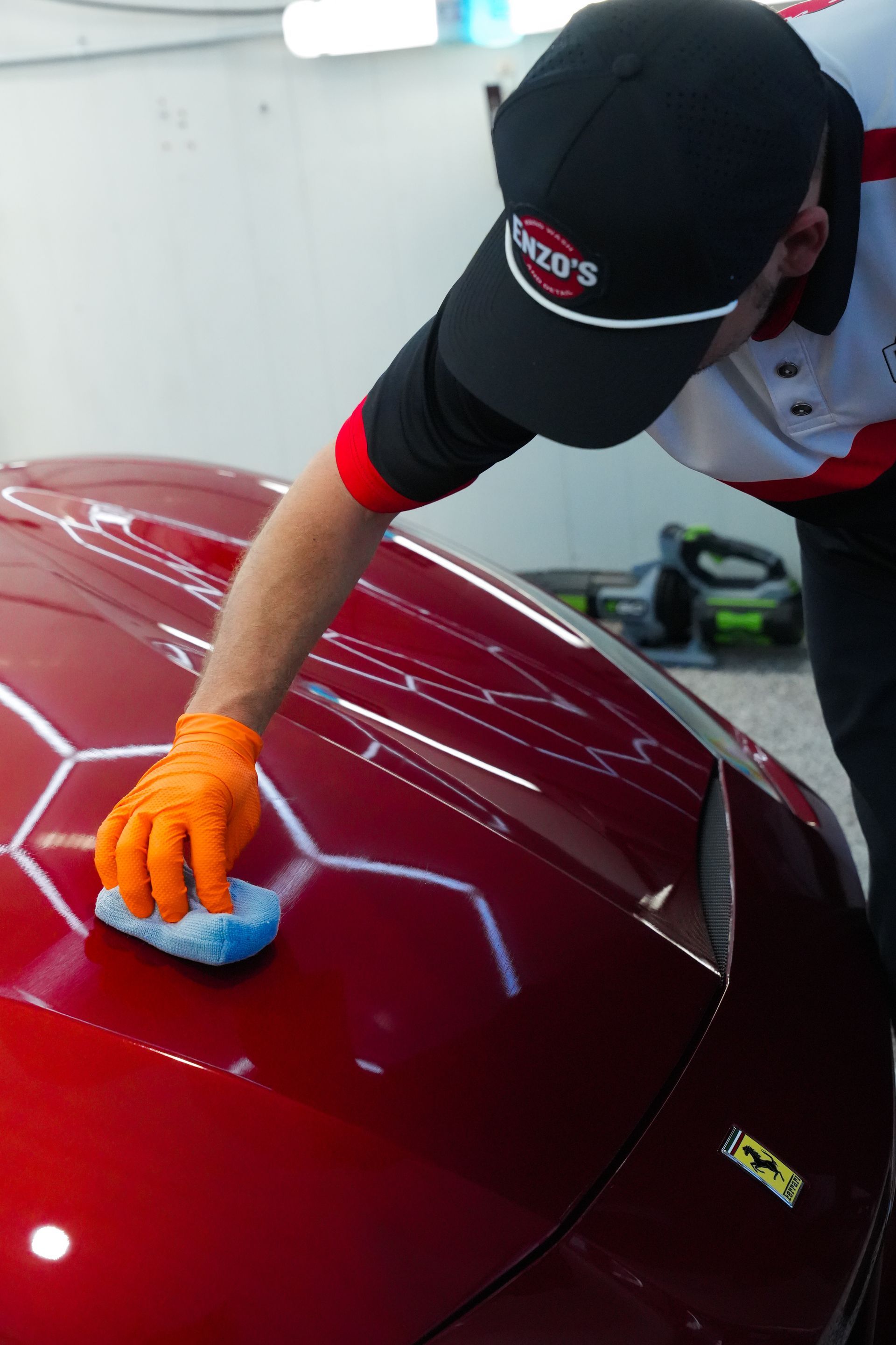 Person wearing orange gloves applying polish to a red car hood.