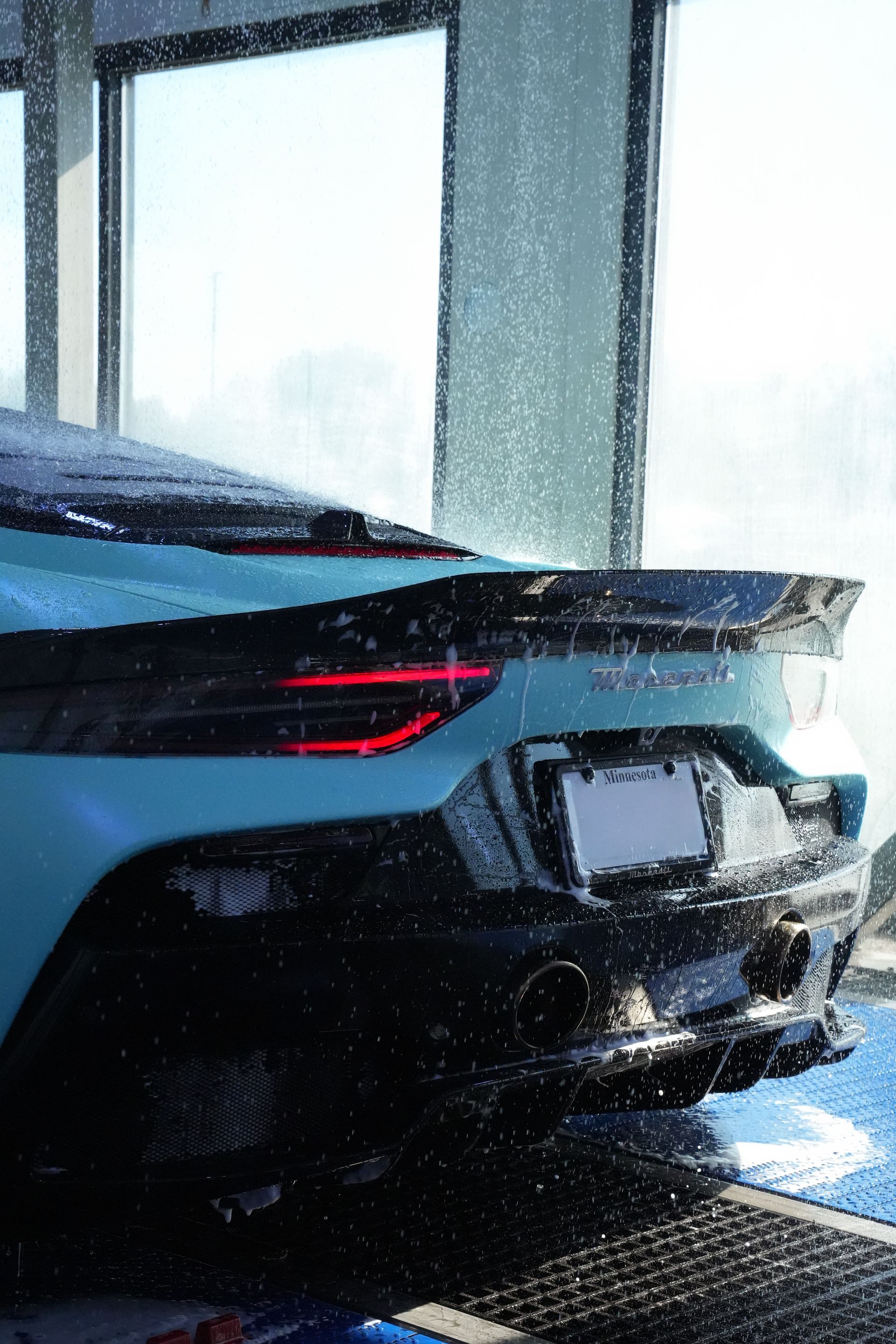Aqua car being washed, water droplets visible. Black spoiler, taillights lit.