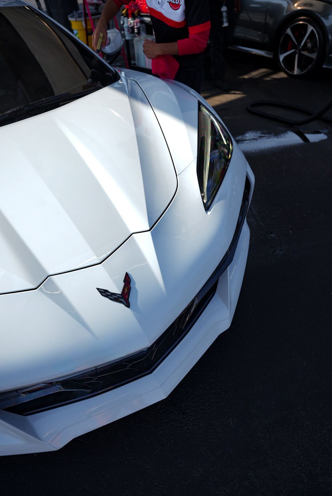 White sports car being washed; person spraying foam.