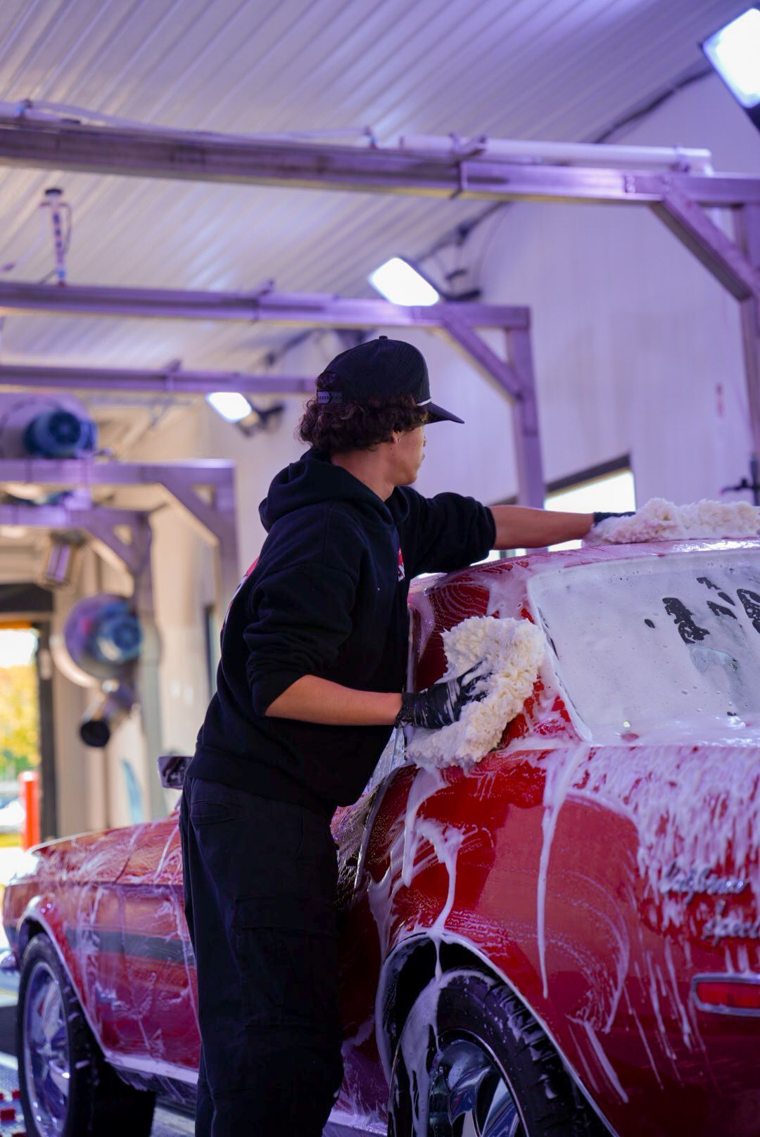 Person washing a red car with soapy foam at a car wash.