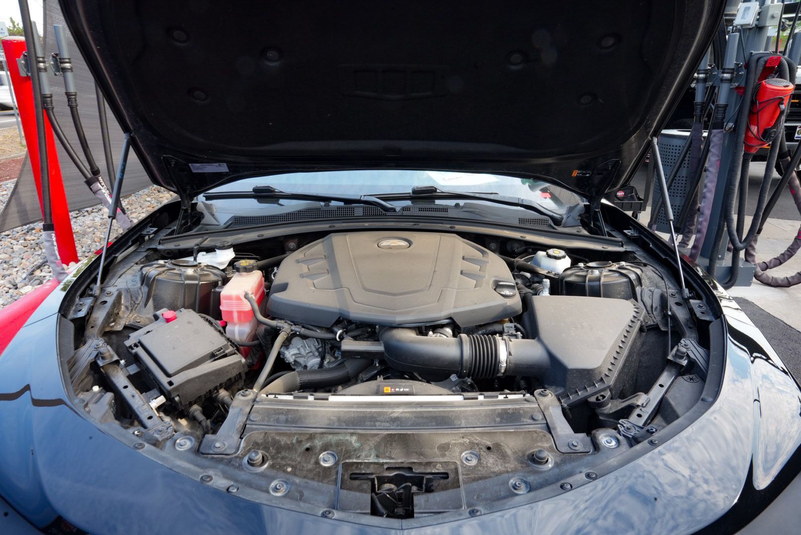 Black car engine compartment open at gas station.