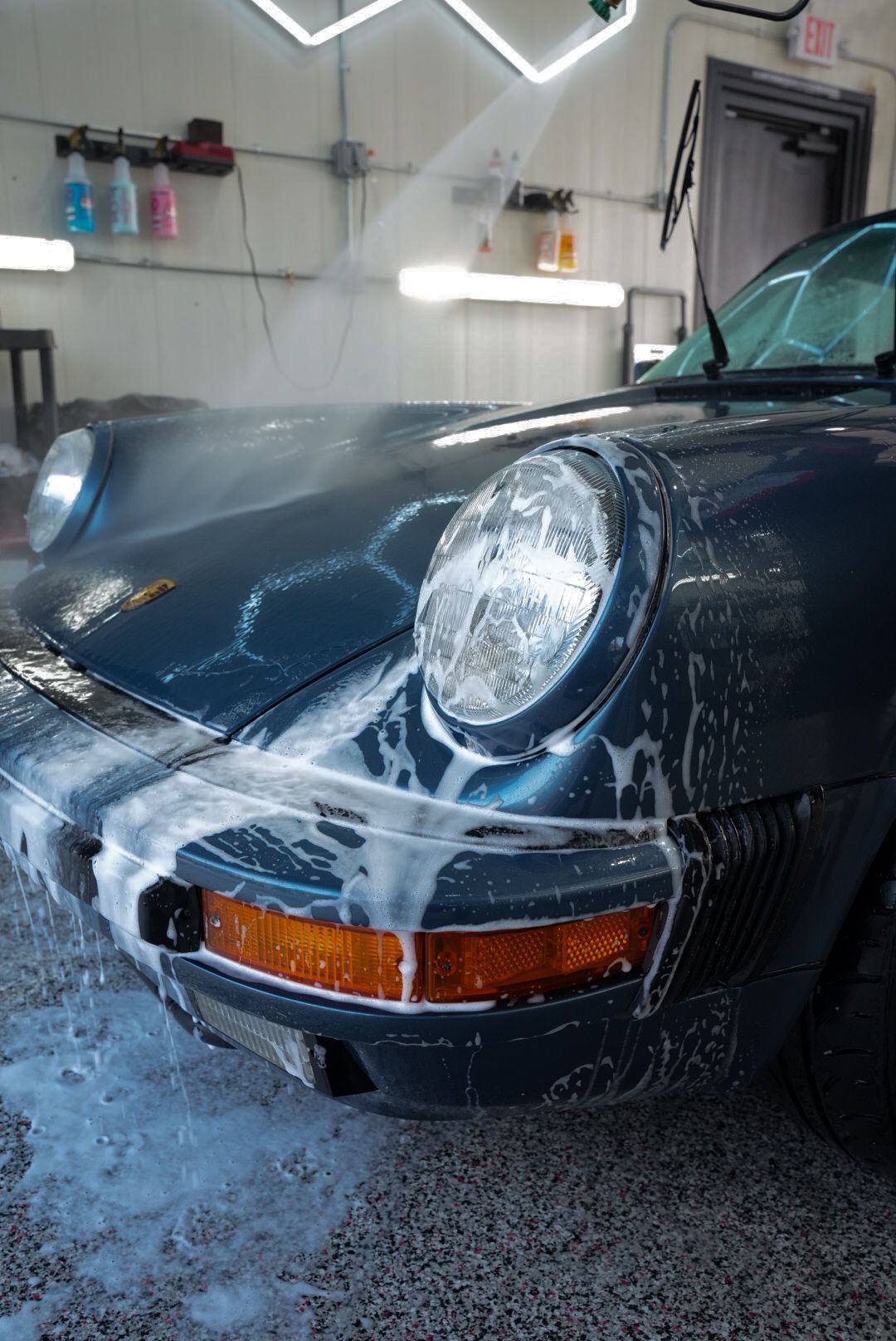 A blue Porsche being washed with soapy water in a garage.