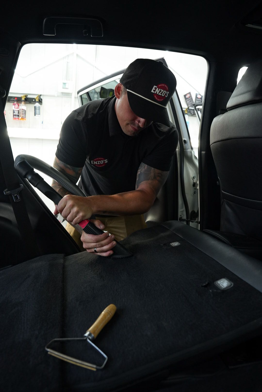 Man cleaning car interior with a tool. He wears a cap and black shirt. A lint roller is visible.