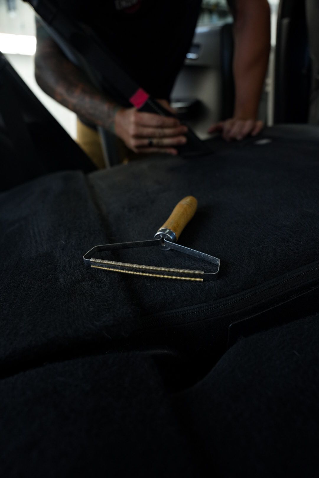 A person using a lint remover on black fabric, with wooden handle and metal blades.