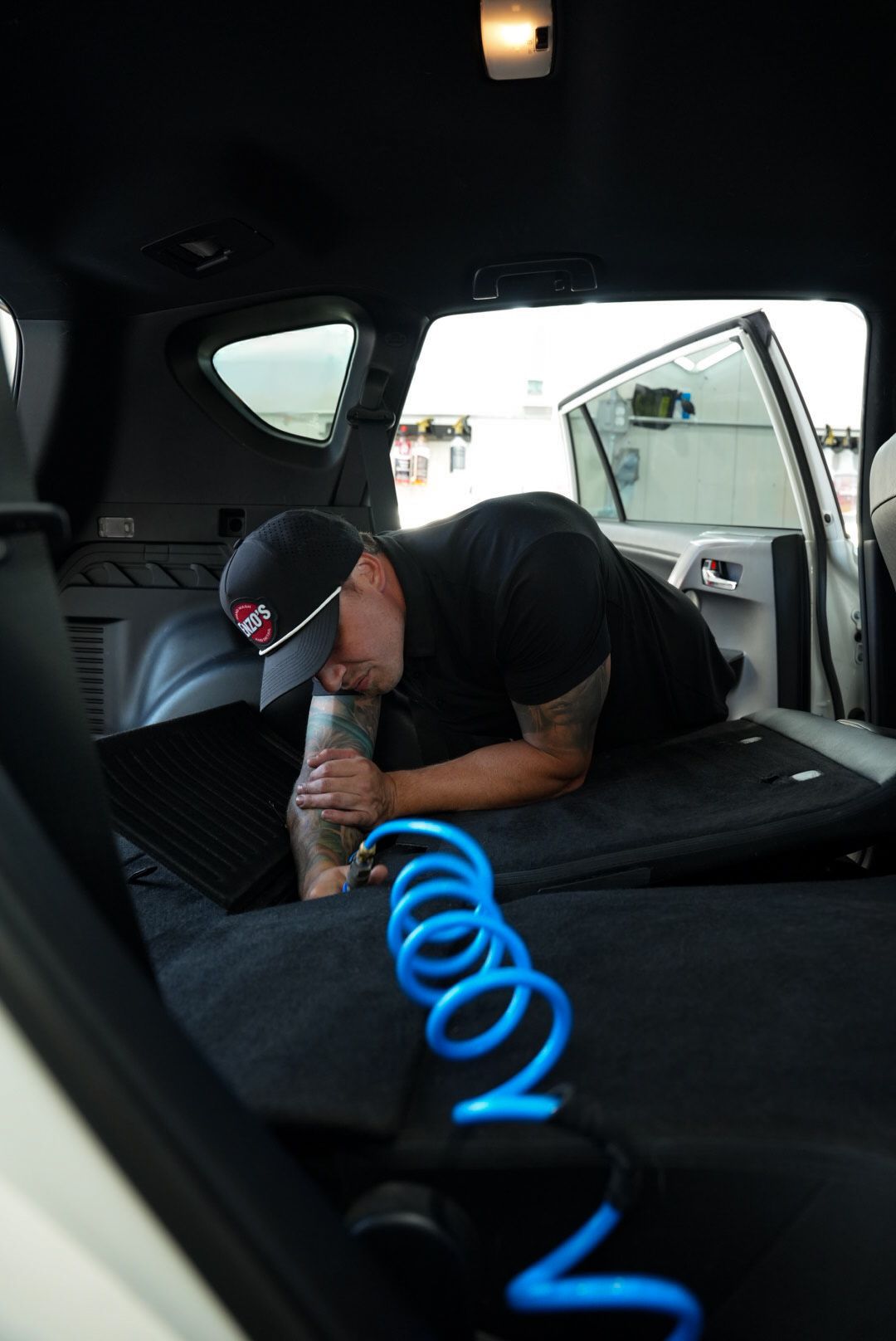 Man working in the open rear of a white vehicle, bent over. Blue hose is in the foreground.