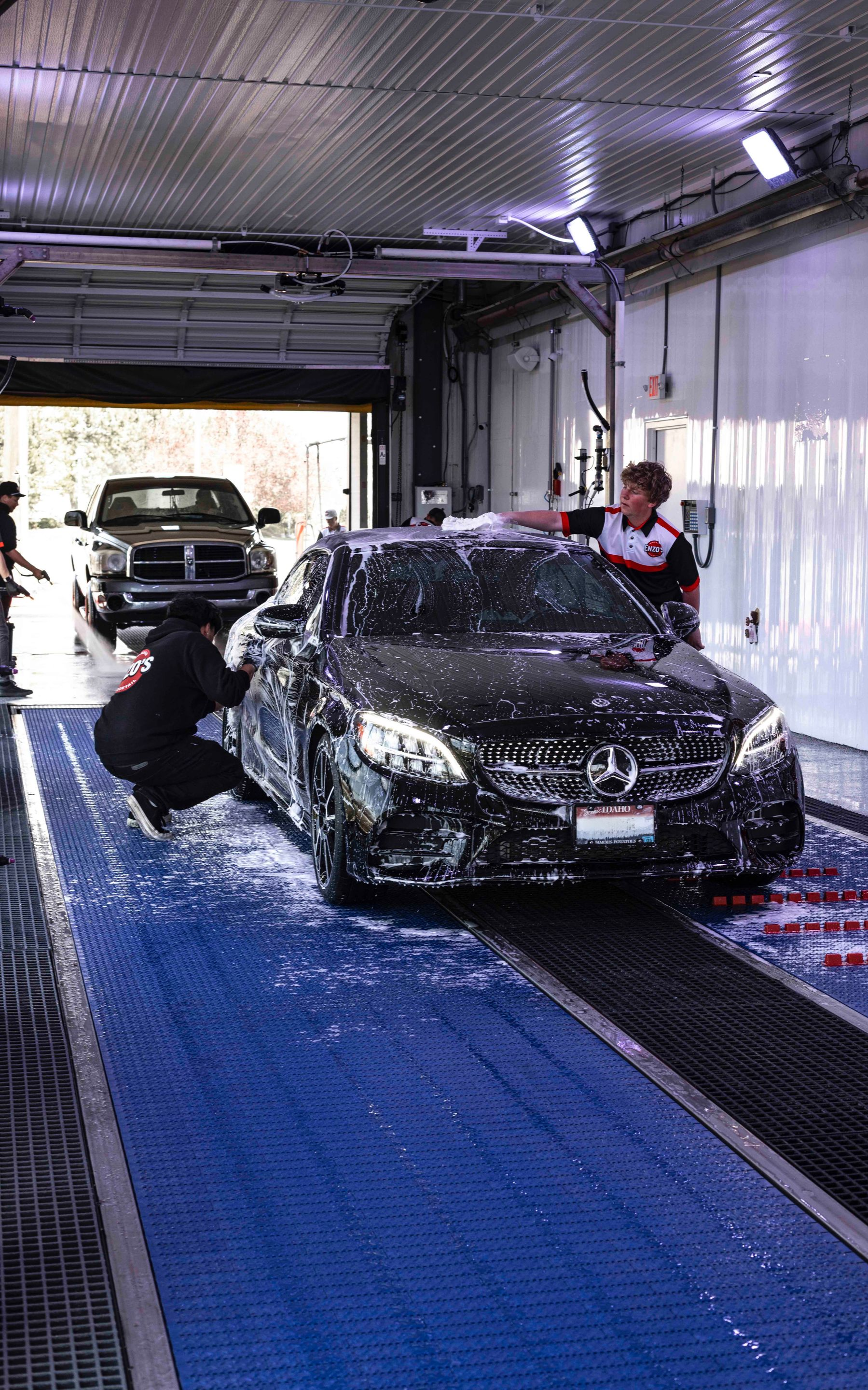Car being washed at a car wash by two workers, soap bubbles cover the car's surface.
