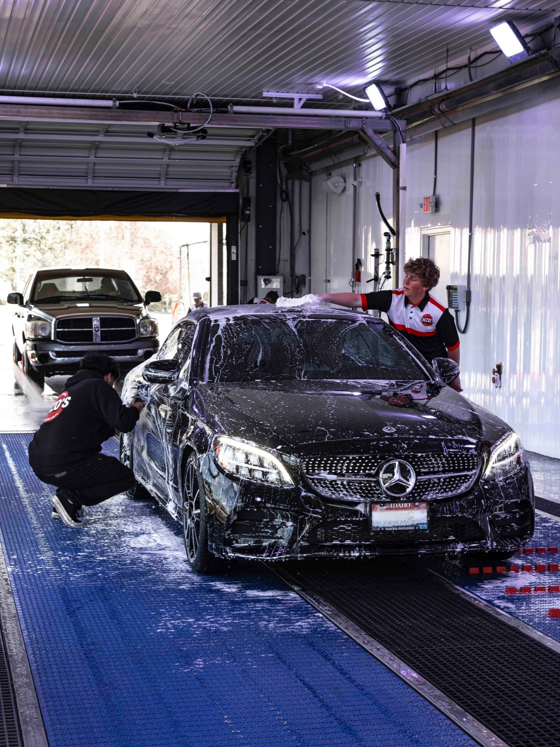 Car wash workers cleaning a black Mercedes in an indoor wash bay
