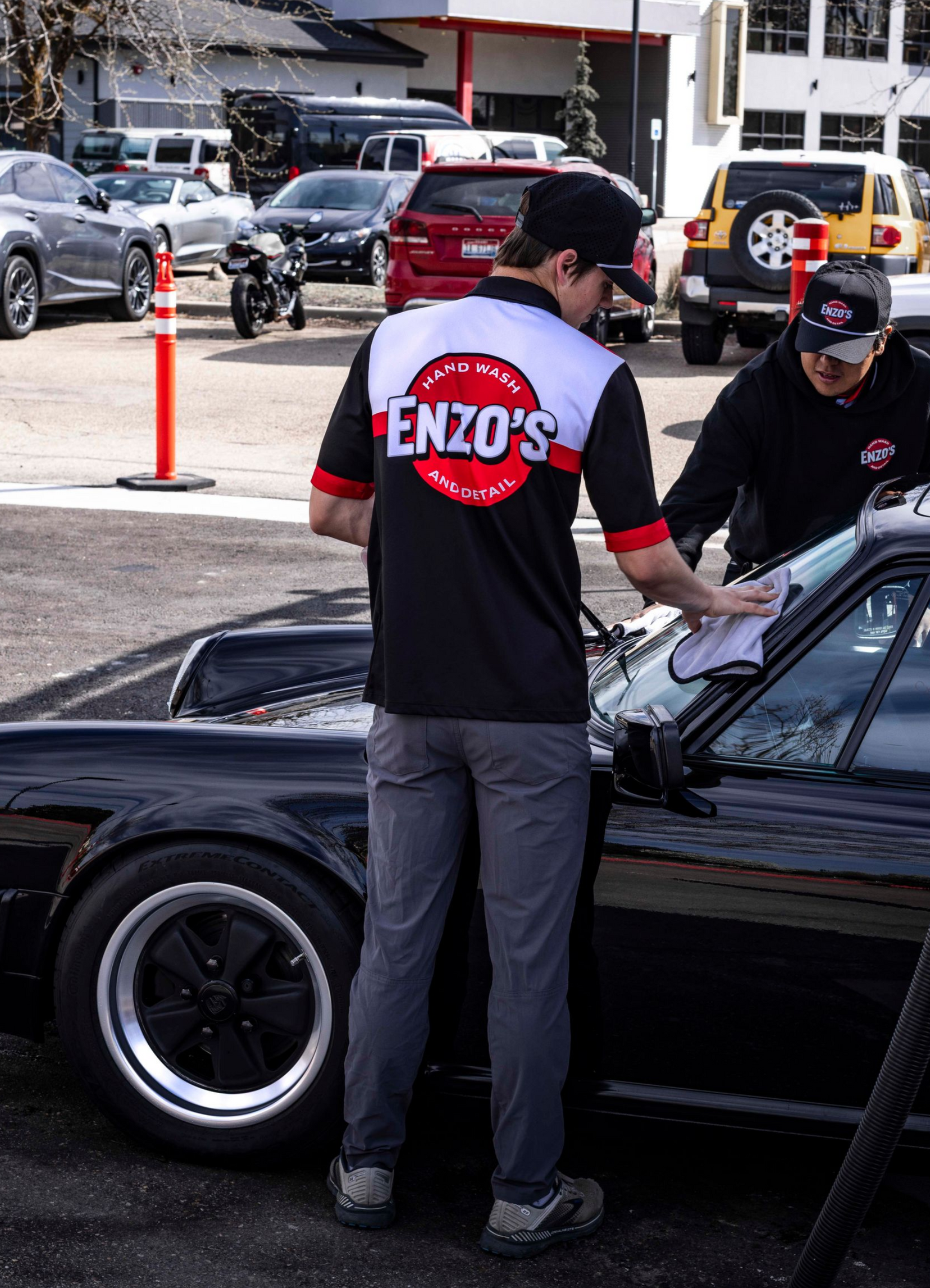 Person washing a black car, using a sponge covered in soap in a brightly lit garage.