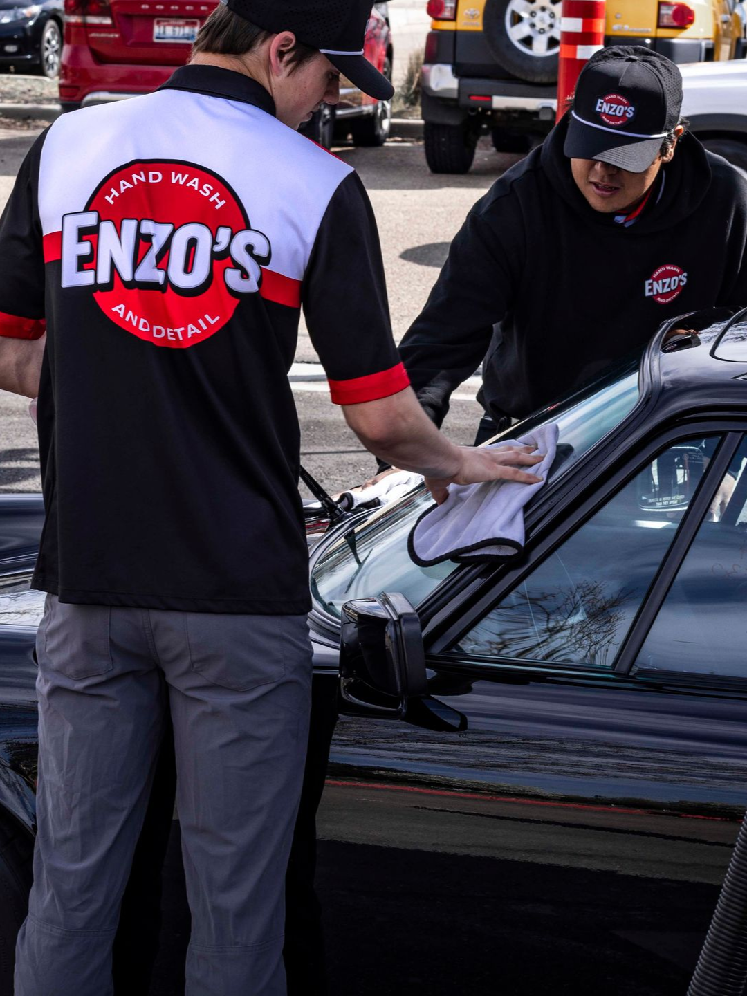 A person wearing black gloves is polishing a black car