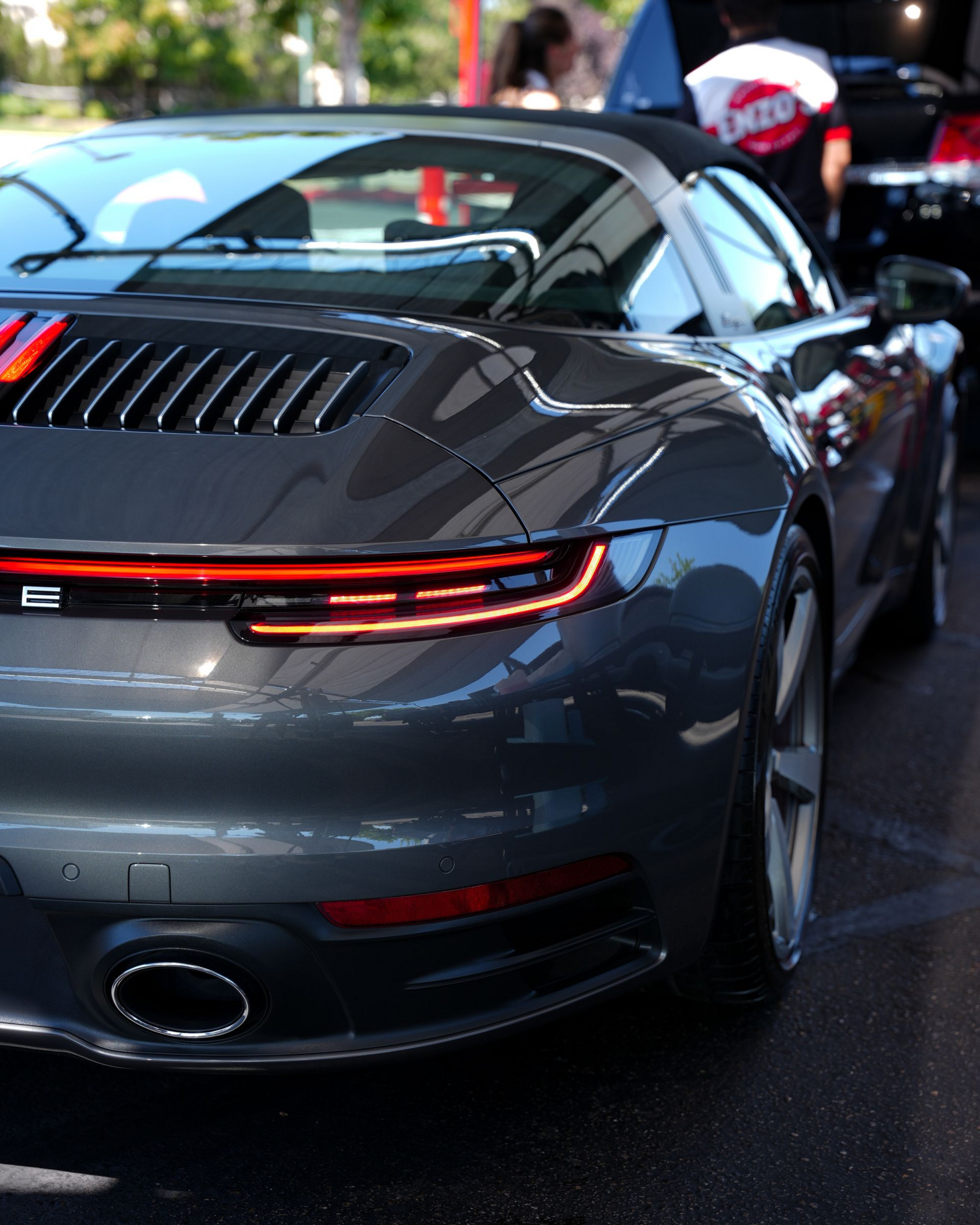 Dark gray Porsche 911 Targa sports car rear view with red taillights and open top.