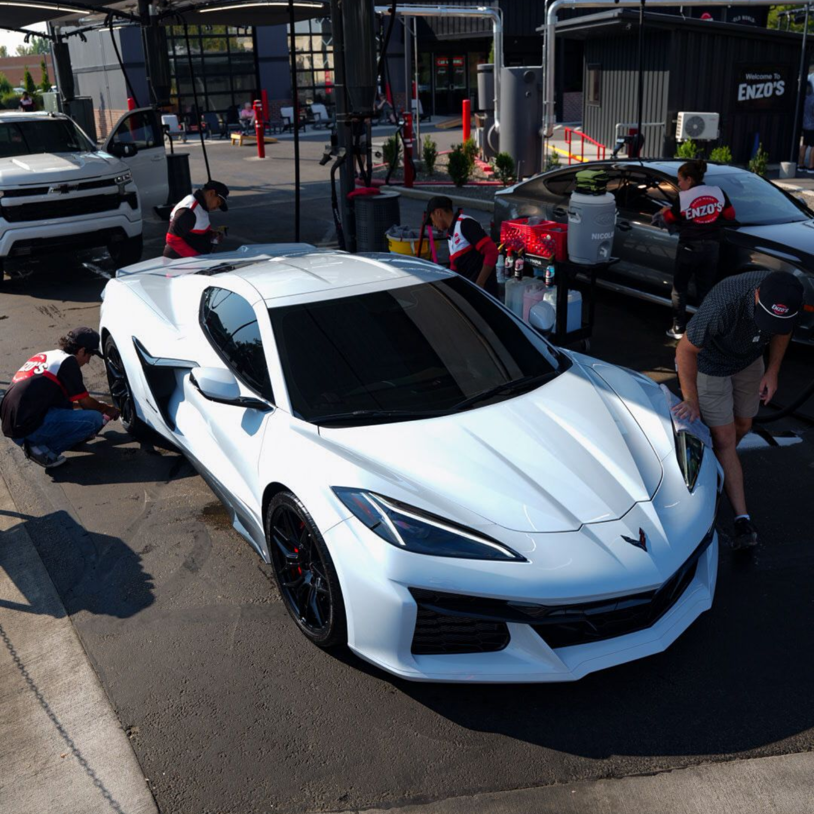 White sports car being cleaned at a car wash by multiple workers.