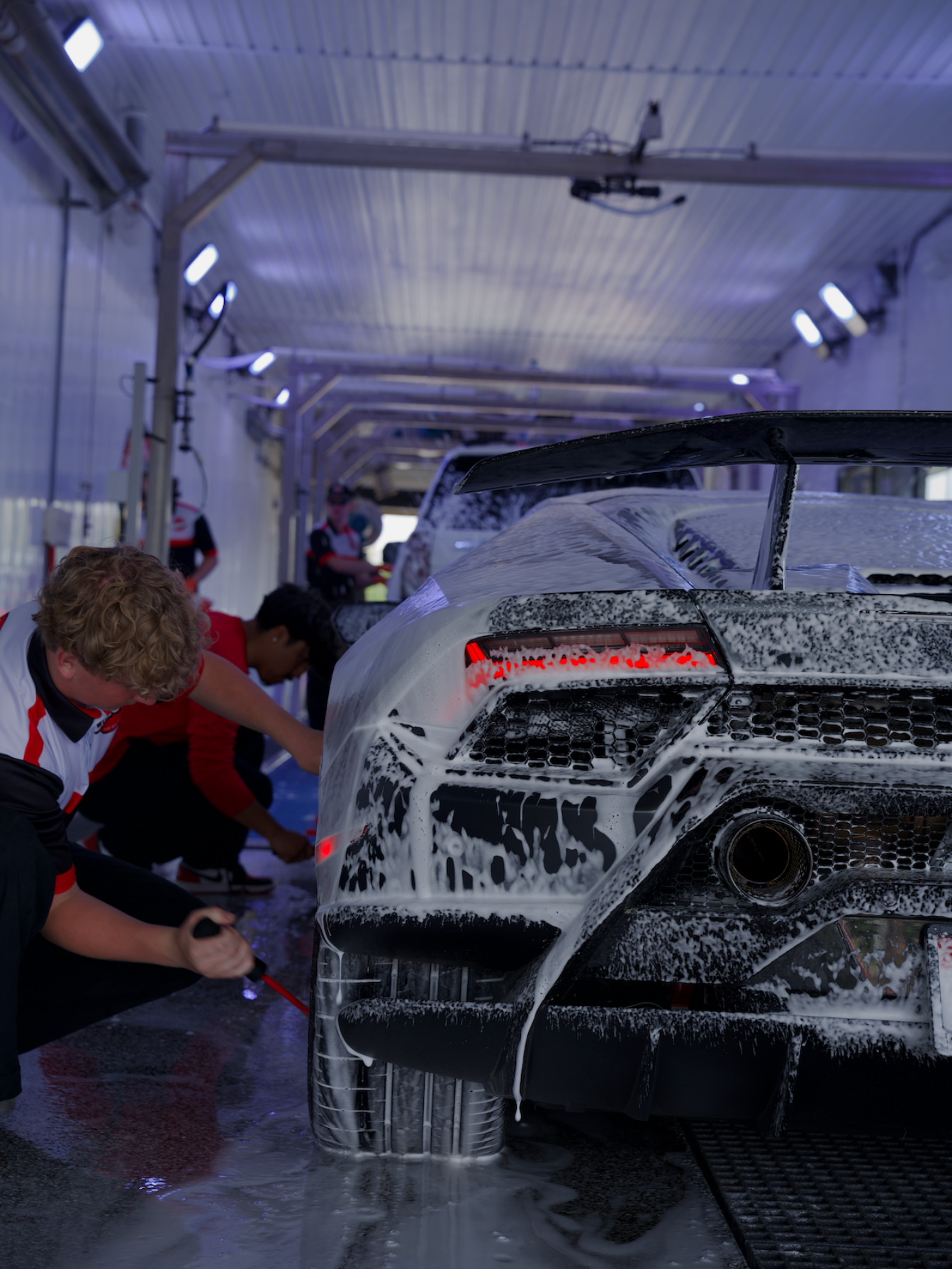 A man is cleaning the wheel of a black car with a sponge.