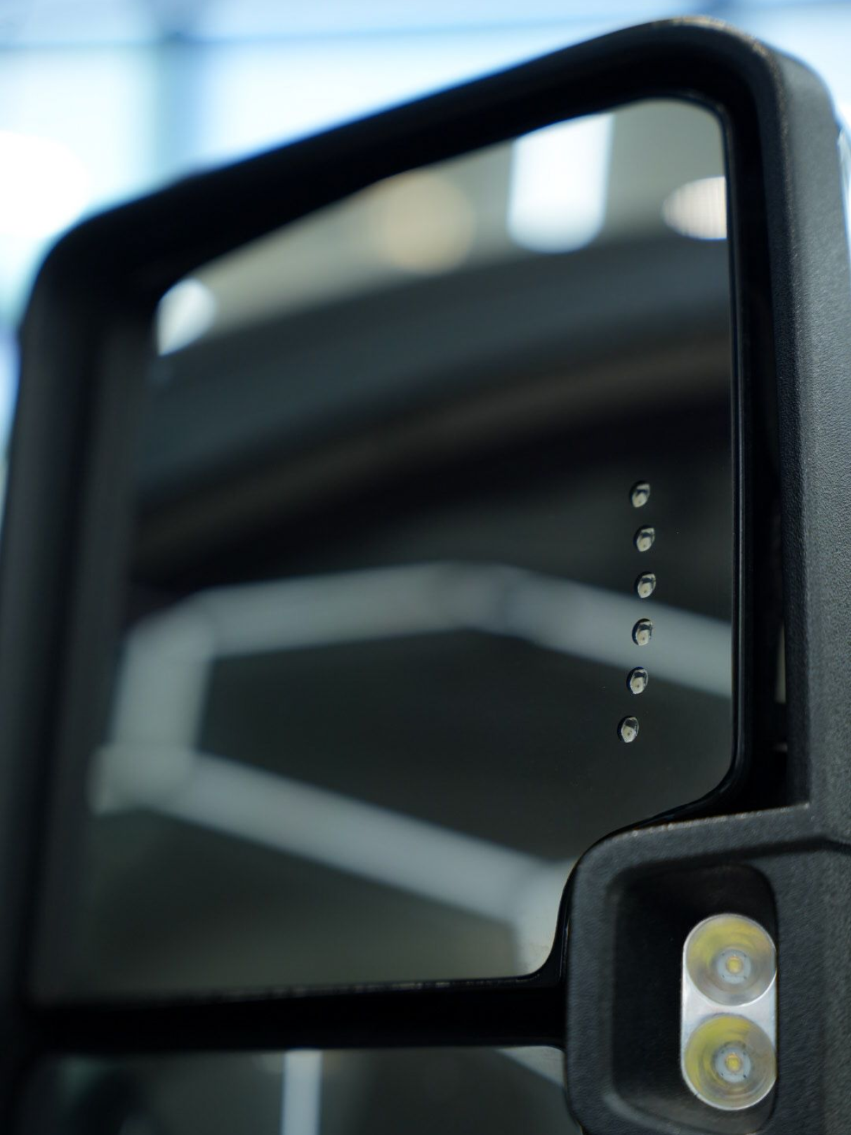Black side-view mirror with blind spot indicator lights and a spotlight on a vehicle.