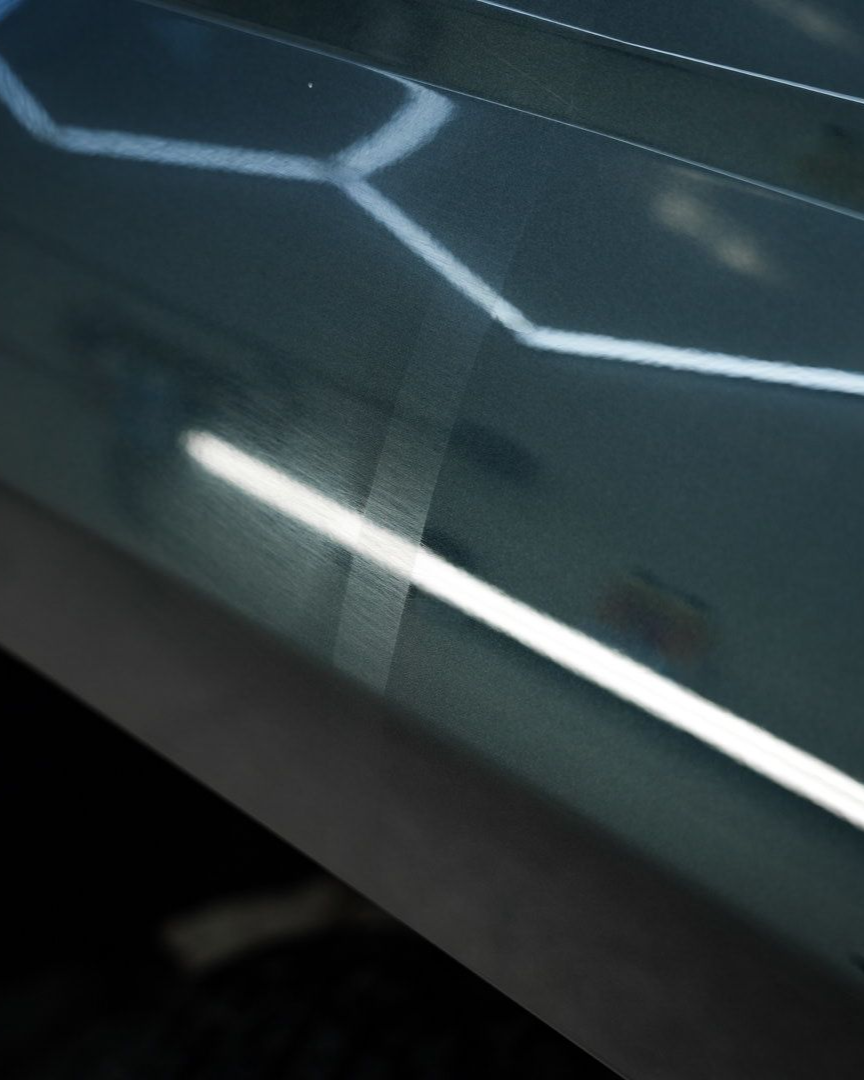 Person using a red and black power buffer on a blue car's exterior.