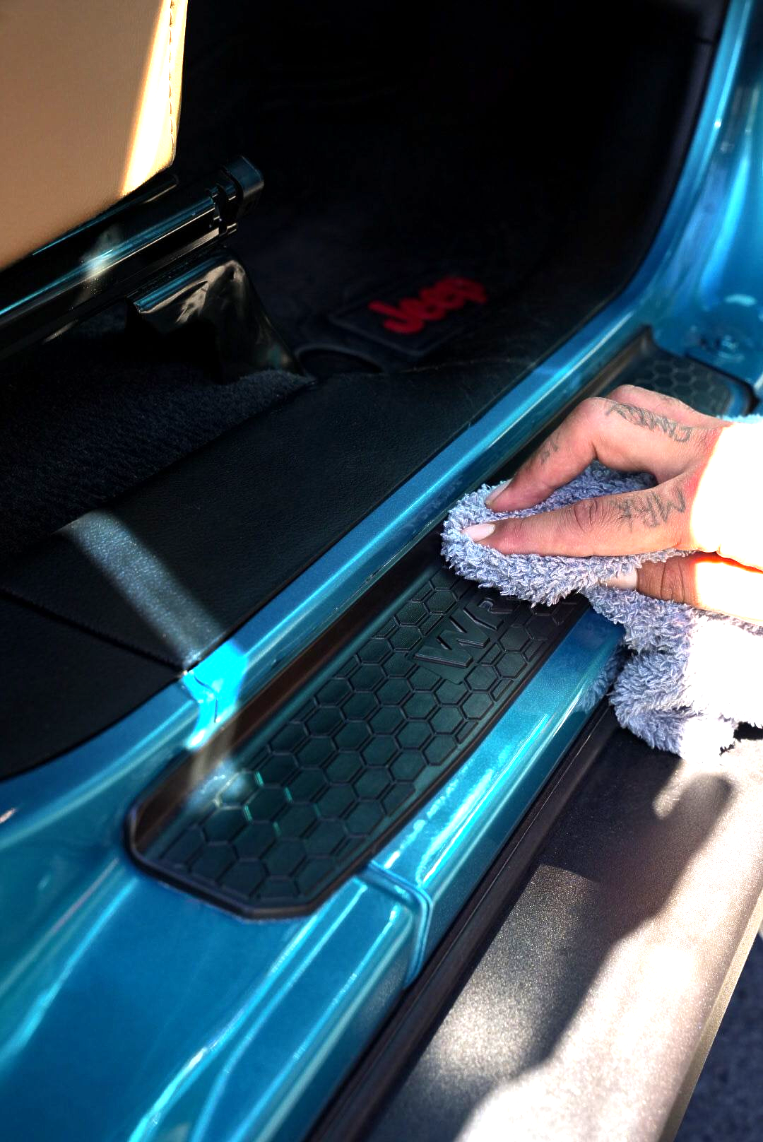 A man is cleaning the wheel of a black car with a sponge.