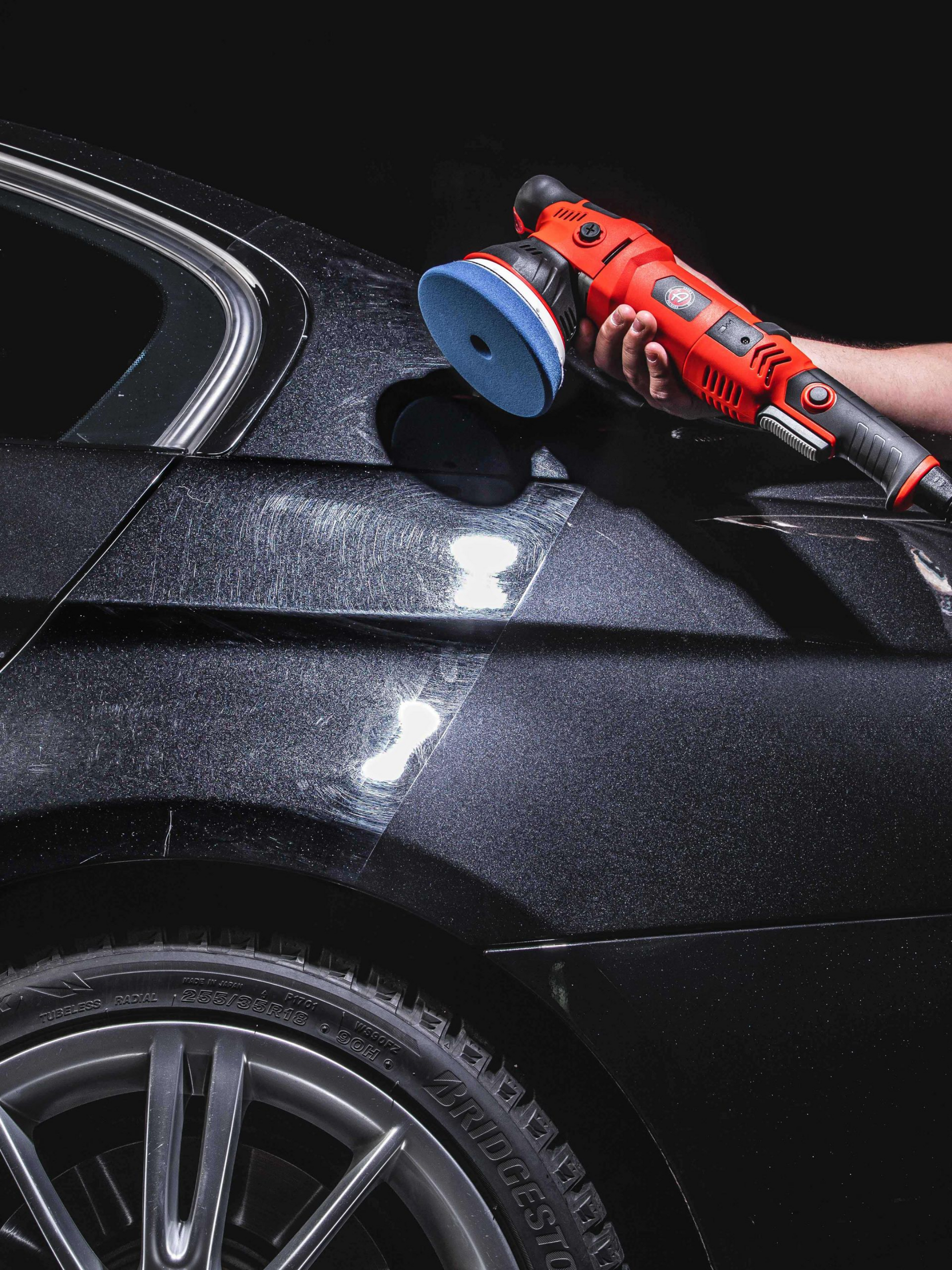 A man is cleaning the wheel of a black car with a sponge.