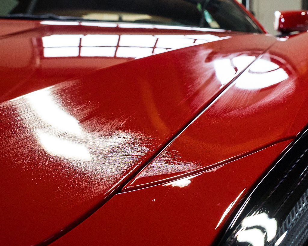 Red car hood with glossy finish reflecting lights.