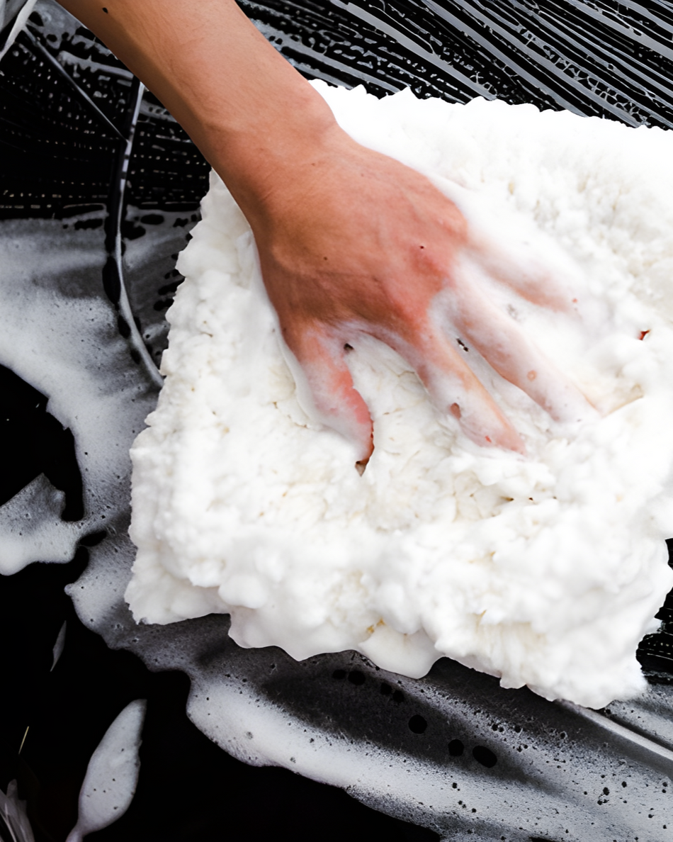 Hand rubbing white foam on a black car hood during washing