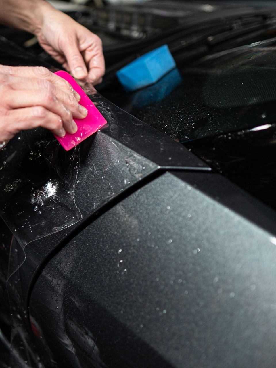 Person washing an orange car at a car wash. They are applying foam to the front bumper.