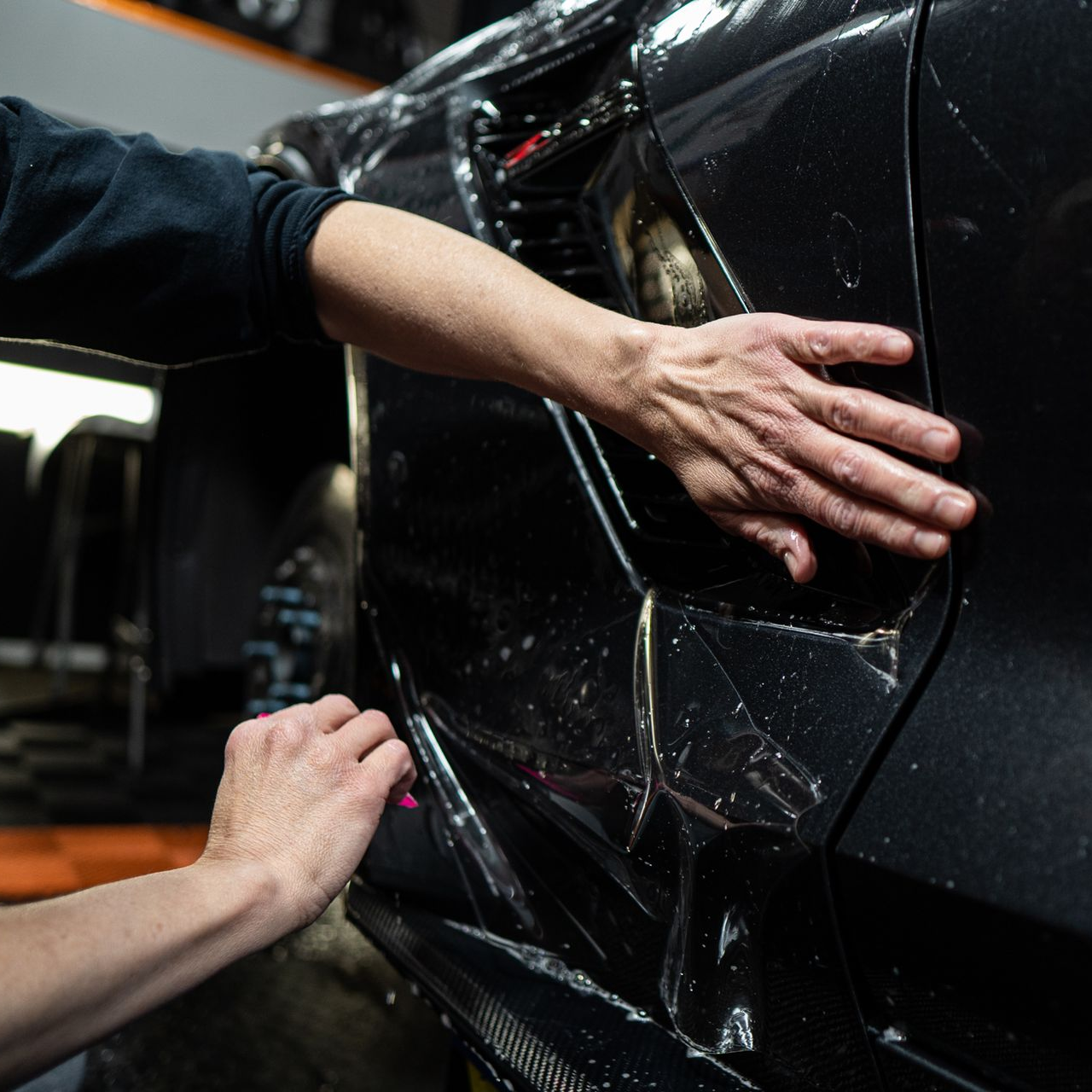 Hands applying clear protective film to the side of a black car.