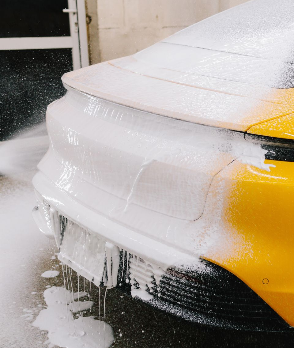 A man is cleaning the wheel of a black car with a sponge.