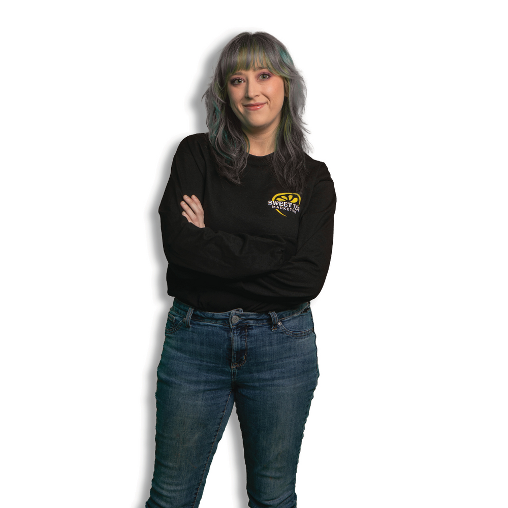 A woman wearing a black sweatshirt and blue jeans is standing with her arms crossed.