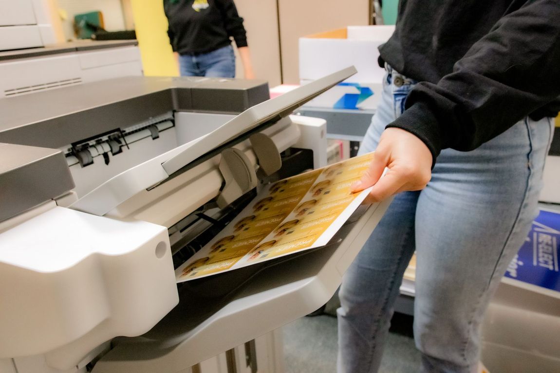 A woman is holding a piece of paper in front of a printer.