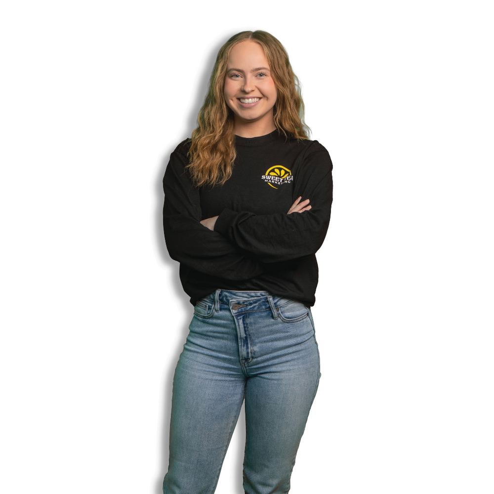 A woman wearing a black sweater and blue jeans is standing with her arms crossed.