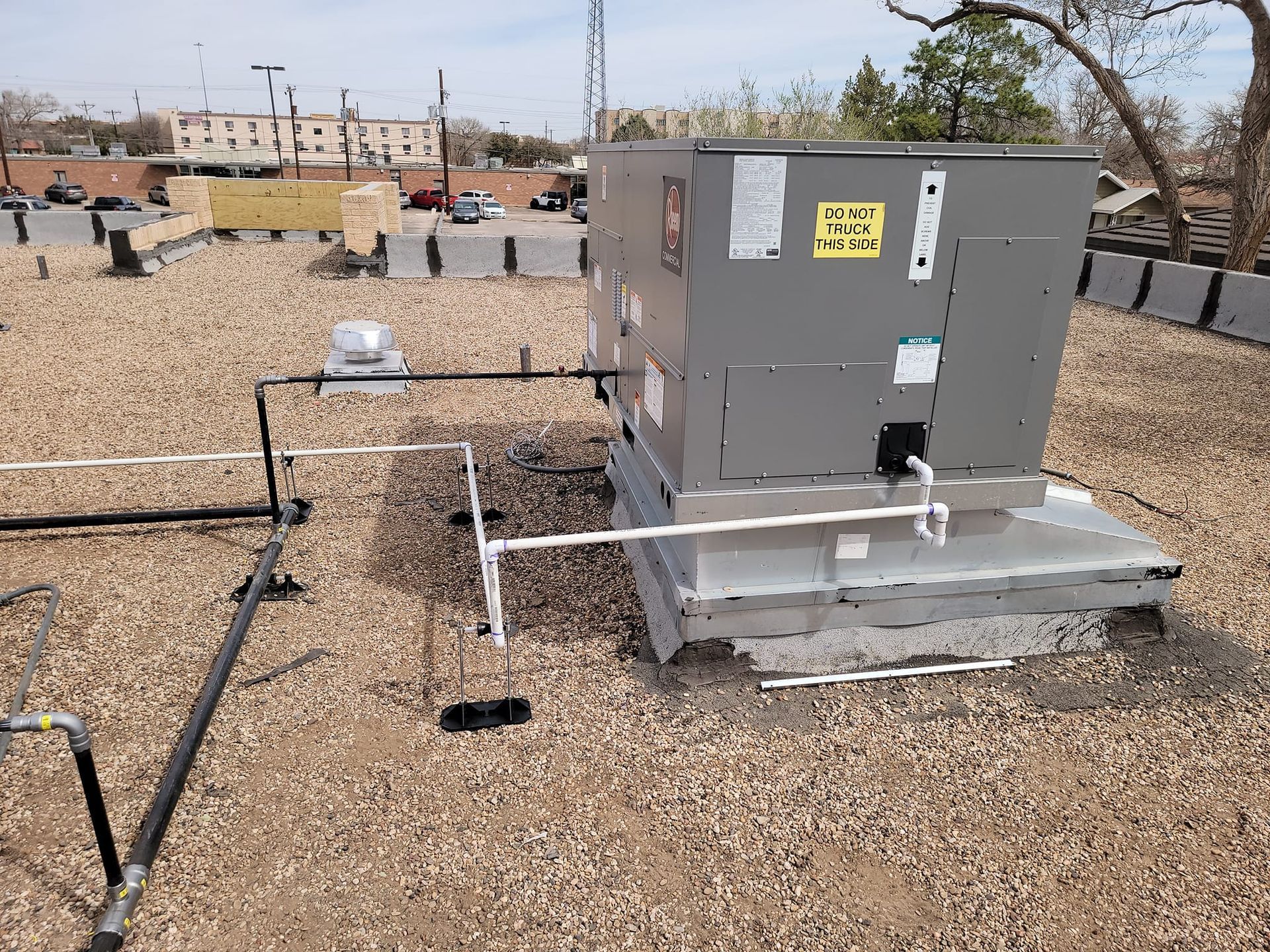 An air conditioner is sitting on top of a gravel covered roof.