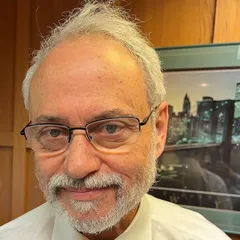 A man with glasses and a beard is smiling in front of a picture.